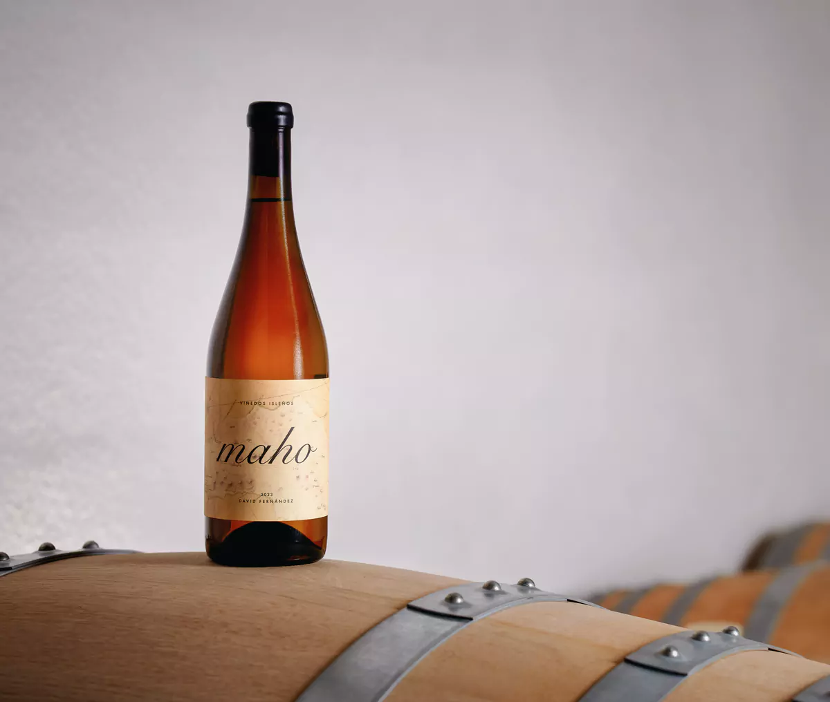 Una botella de Maho apoyada sobre una barrica de roble